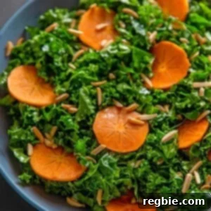 An overhead shot of two hands holding a large blue bowl filled with kale salad and persimmons and toasted almonds, a simple and delicious winter salad.