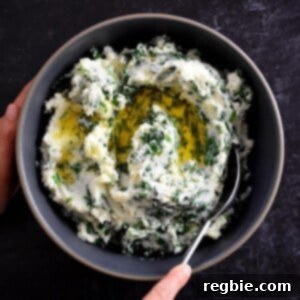 A hand is scooping paleo cauliflower colcannon from a gray bowl. The colcannon is white pureed cauliflower with flecks of green kale and scallions in it. There is melted ghee on top.