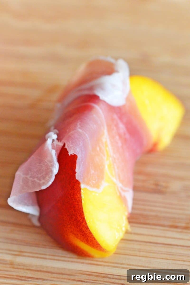 A close-up shot of a slice of peach wrapped with a thin slice of prosciutto.