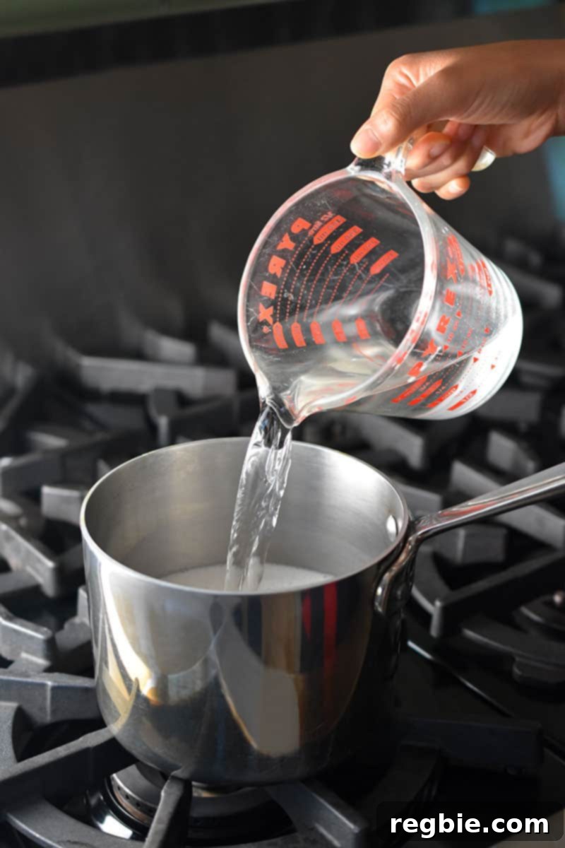 Paleo Dairy-Free Golden Turmeric Elixir 4 Pouring water from a Pyrex measuring cup into a saucepan on the stovetop to make Golden Milk.
