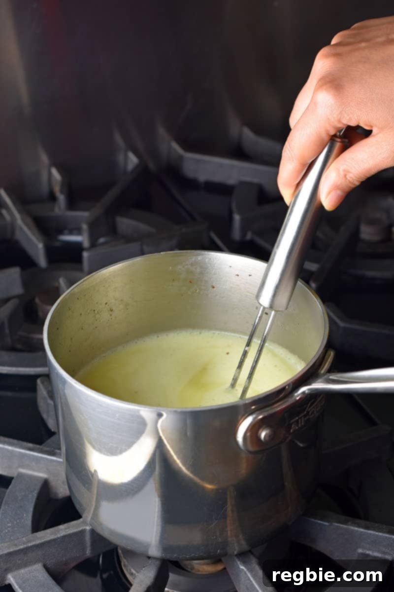 Paleo Dairy-Free Golden Turmeric Elixir 5 Someone is whisking a small stainless steel saucepan filled with golden milk.