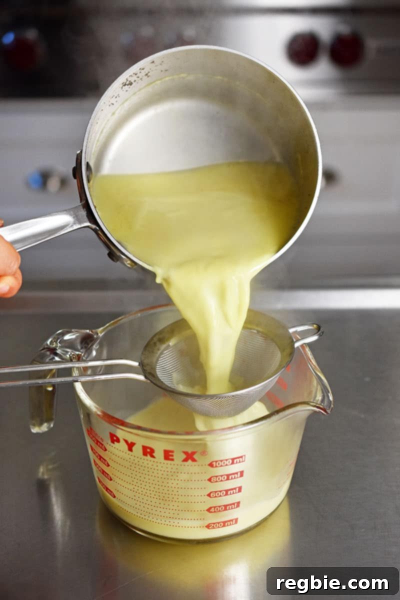 Paleo Dairy-Free Golden Turmeric Elixir 6 Pouring the Golden Milk from a small saucepan through a fine mesh sieve into a 4-cup Pyrex liquid measuring cup.