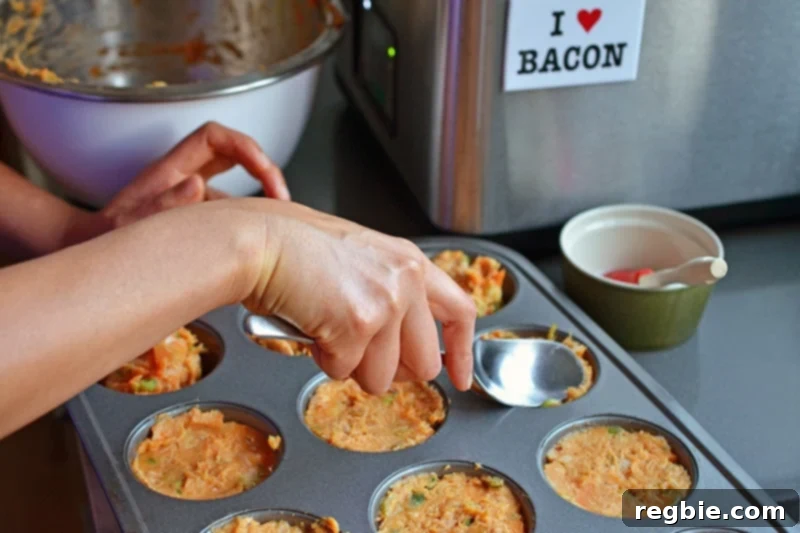Someone flattening the spicy tuna cake mixture into a muffin pan with the back of a spoon.