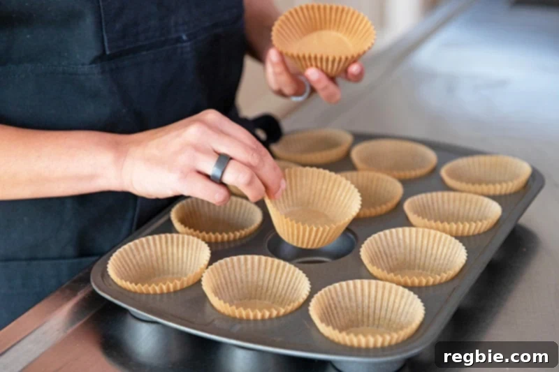 A person is adding parchment muffin liners to a muffin tin.