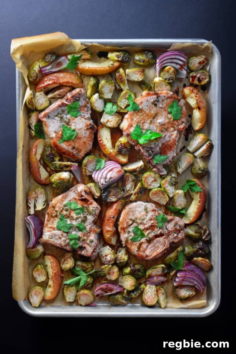 Overhead shot of a rustic sheet pan pork chop supper, featuring roasted pork chops, apples, and Brussels sprouts.