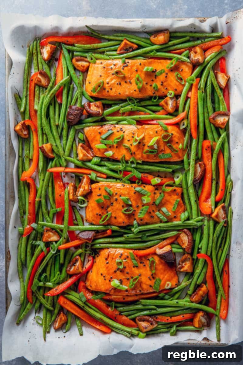 An overhead shot of Whole30 and paleo Teriyaki Salmon Sheet Pan, featuring four perfectly cooked salmon fillets surrounded by vibrant green beans and bell peppers.