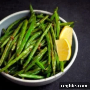 A bowl filled with roasted green beans with lemon and garlic and two lemon slices.