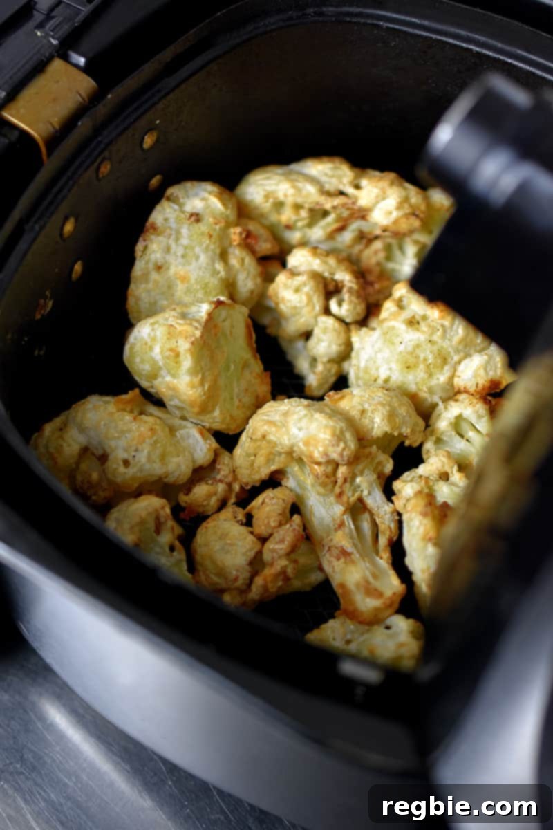 An overhead view of perfectly golden-brown Buffalo Cauliflower in an air fryer basket, now crispy and ready to be coated with the delicious buffalo sauce.