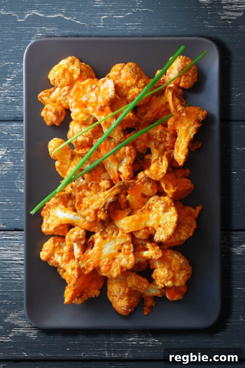 An overhead shot of perfectly baked buffalo cauliflower elegantly arranged on a rectangular gray plate, garnished with three delicate chives on top for a fresh accent.