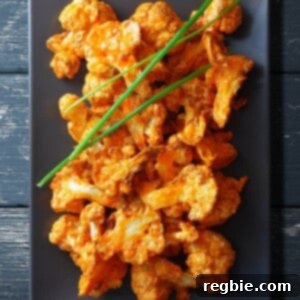 An overhead shot of baked buffalo cauliflower on a rectangular gray plate, garnished with chives, presenting a delicious and healthy appetizer.