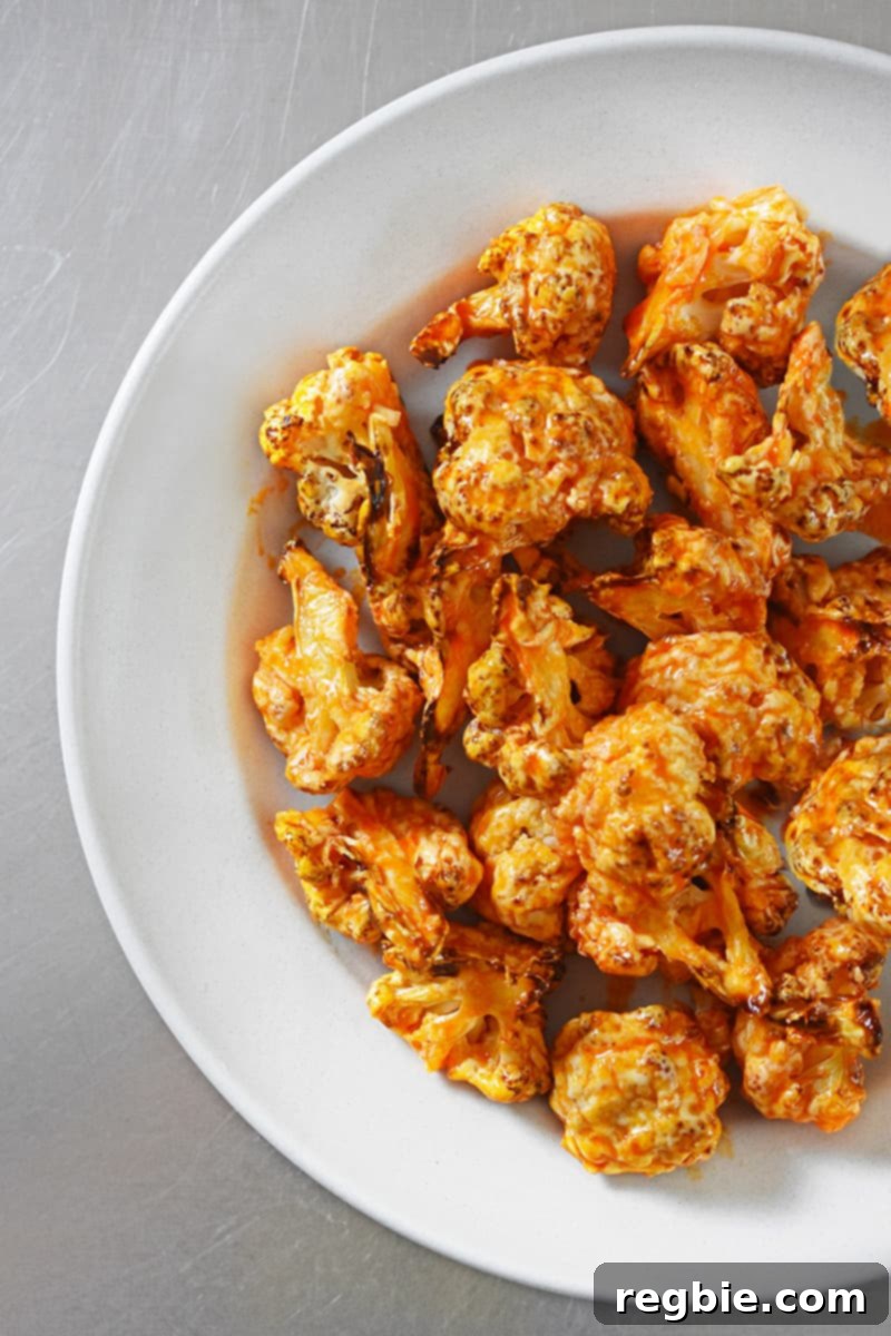 Overhead shot of perfectly baked buffalo cauliflower arranged appealingly in a white round platter, ready for serving. The golden-brown florets showcase the crispy coating.