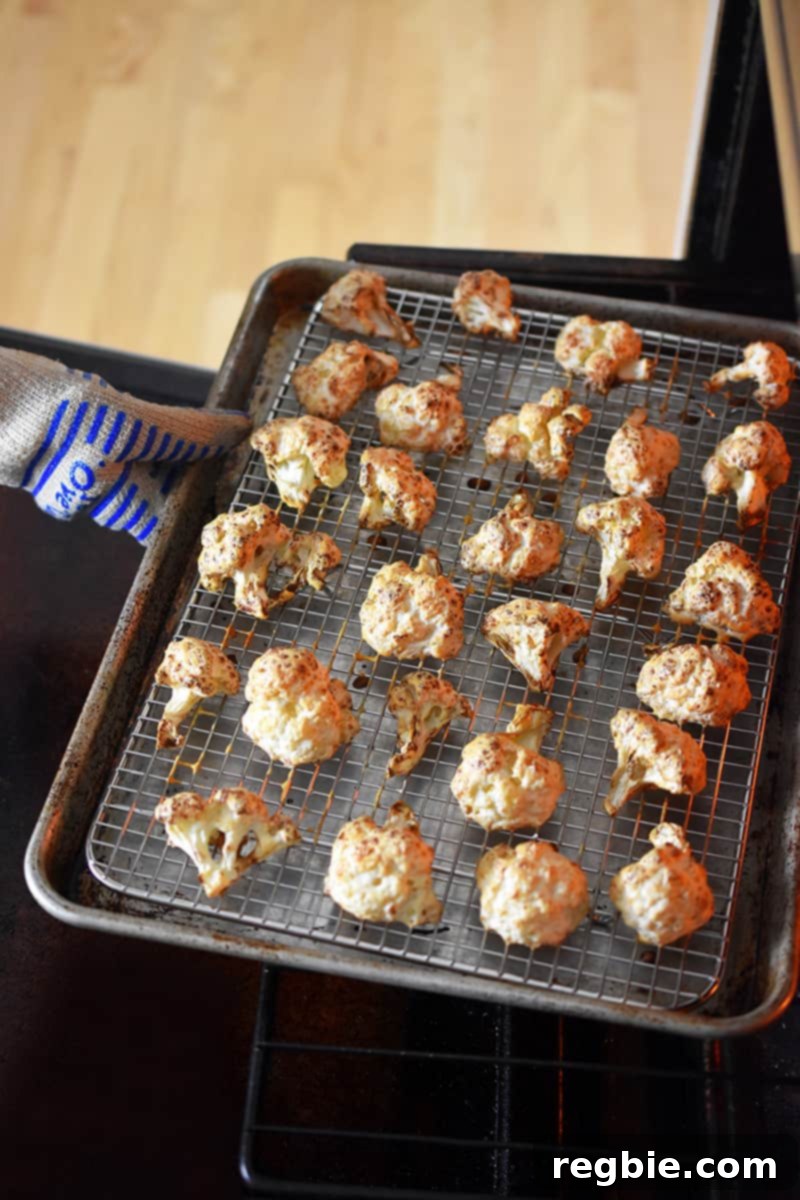 A gloved hand carefully removing a tray of golden brown, crispy Baked Buffalo Cauliflower from the hot oven, highlighting the perfect texture achieved.