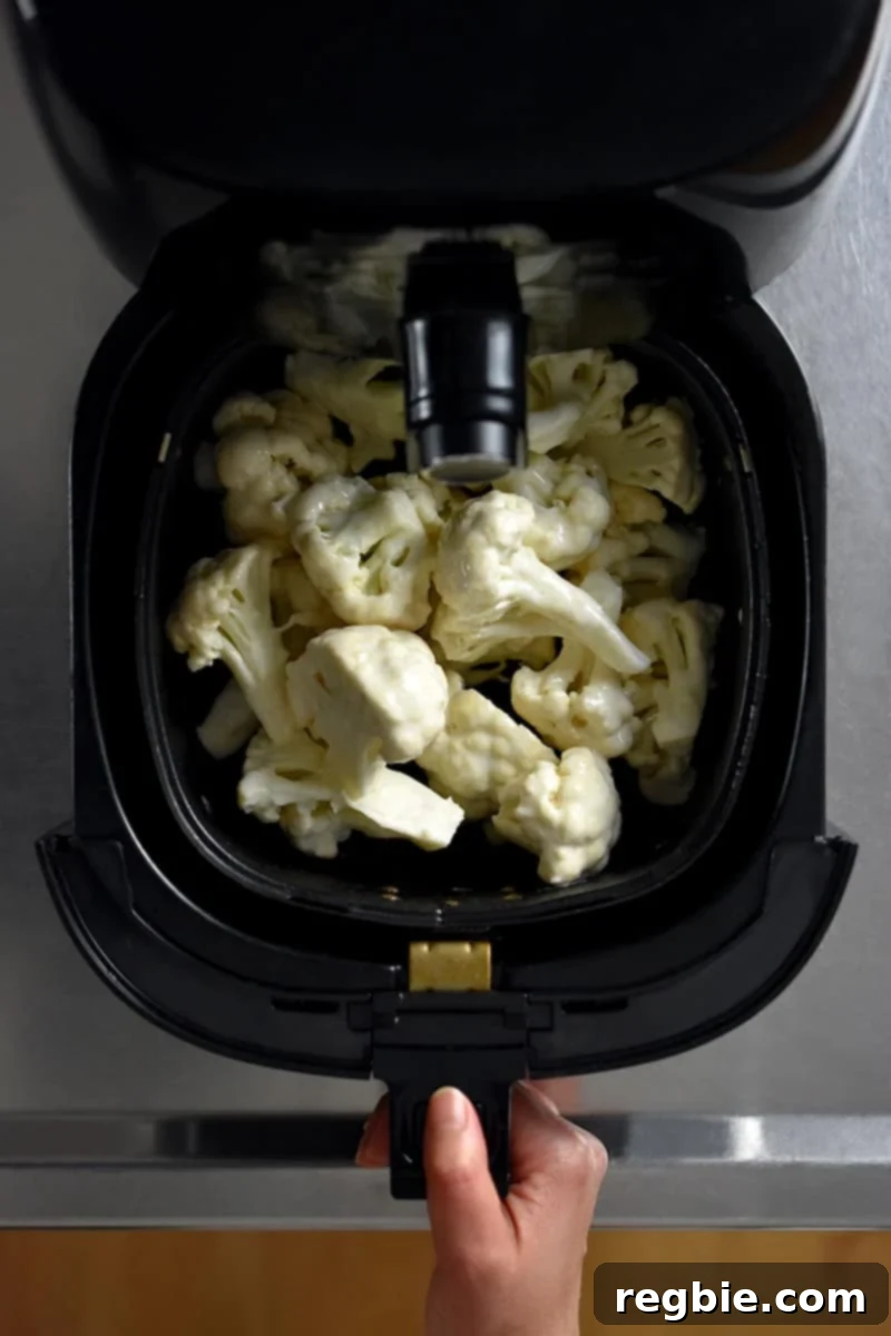 An overhead shot of Buffalo Cauliflower florets meticulously arranged in a single layer within an air fryer basket, prepped and ready for cooking.