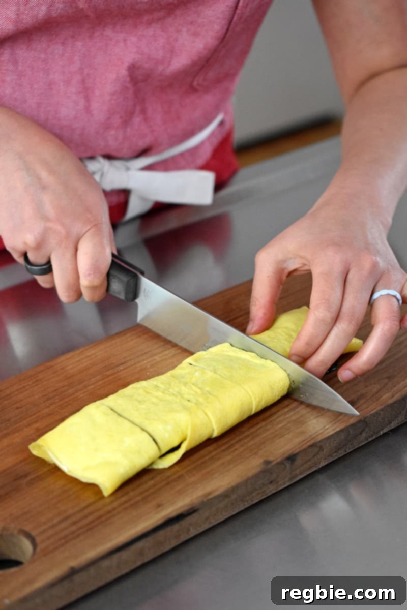 Someone in a red apron is slicing a Korean egg roll with seaweed on a wooden cutting board.