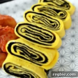 A closeup shot of a cut up Korean Egg Roll Omelet with Roasted Seaweed on a white plate with gray flowers. You can see the spirals of egg and bright yellow egg in the cut-up pieces.