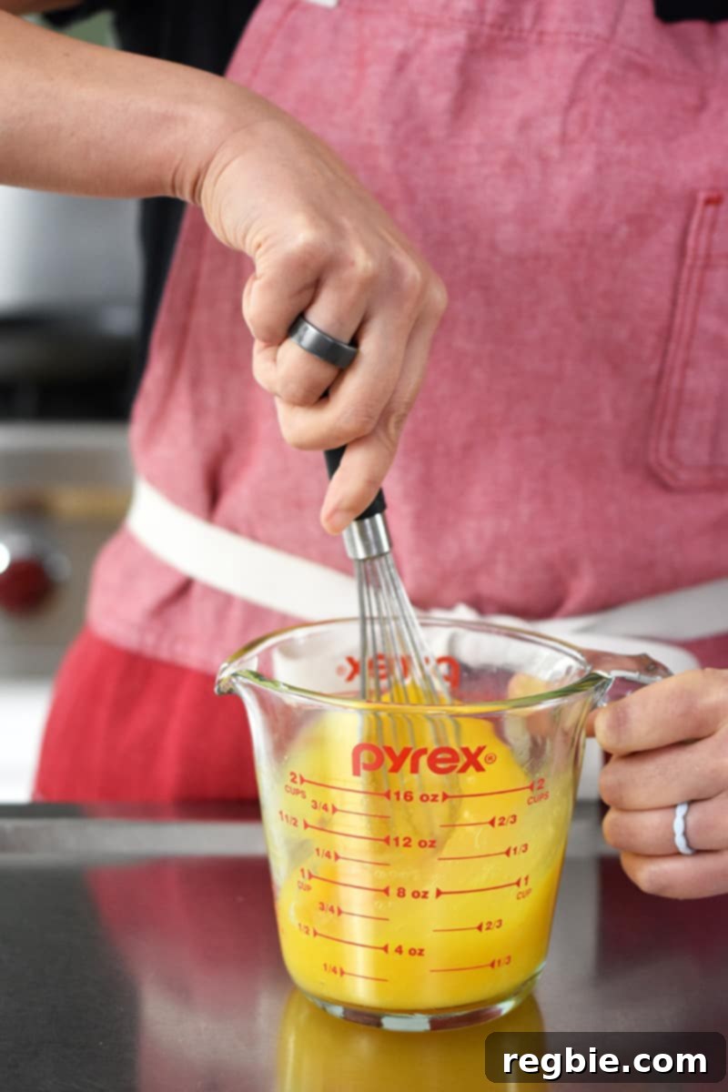 A person in a red apron is whisking eggs and salt in a 2-cup Pyrex glass measuring cup.