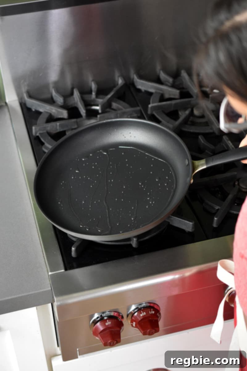 A 12-inch non-stick skillet is being tipped on a gas stovetop to swirl the oil inside.