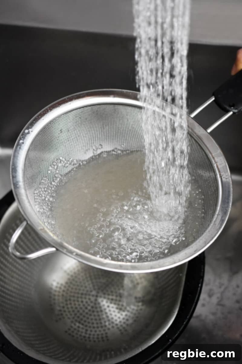 Tropical Mango Coconut Tapioca 11 Running water is being poured into a fine mesh sieve filled with cooked small tapioca pearls.
