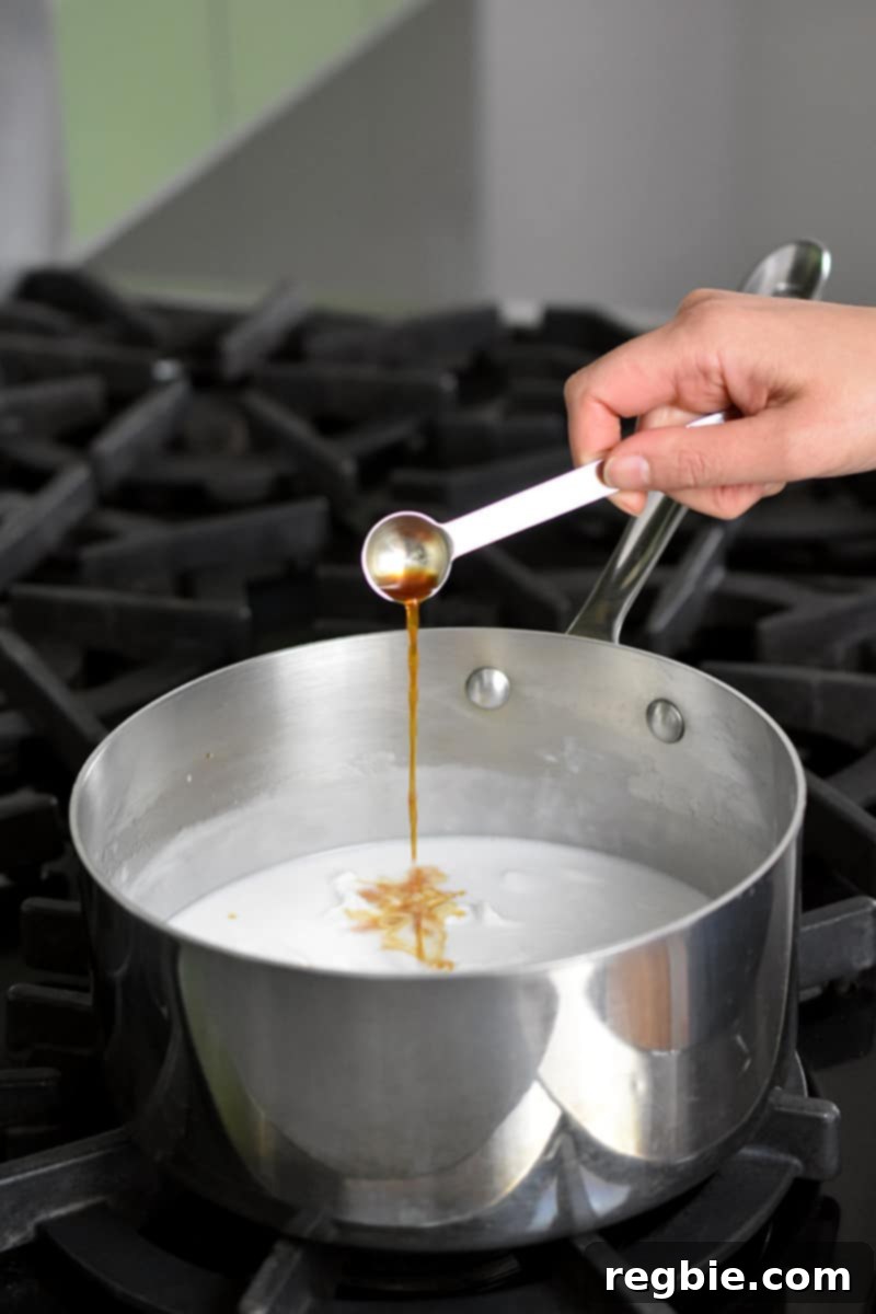 Tropical Mango Coconut Tapioca 12 A hand is adding vanilla extract from a measuring spoon into a saucepan filled with coconut milk.