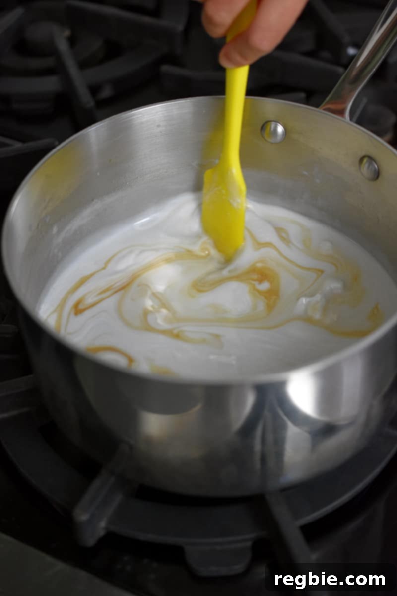 Tropical Mango Coconut Tapioca 13 A yellow spatula is stirring the contents of a saucepan filled with coconut milk, honey, vanilla extract, and salt.