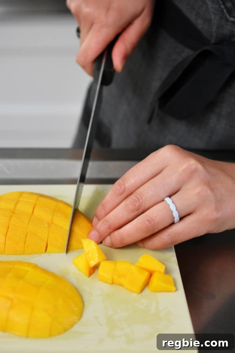 Tropical Mango Coconut Tapioca 18 A closeup of someone cutting peeled mango into cubes on a rubber cutting board.