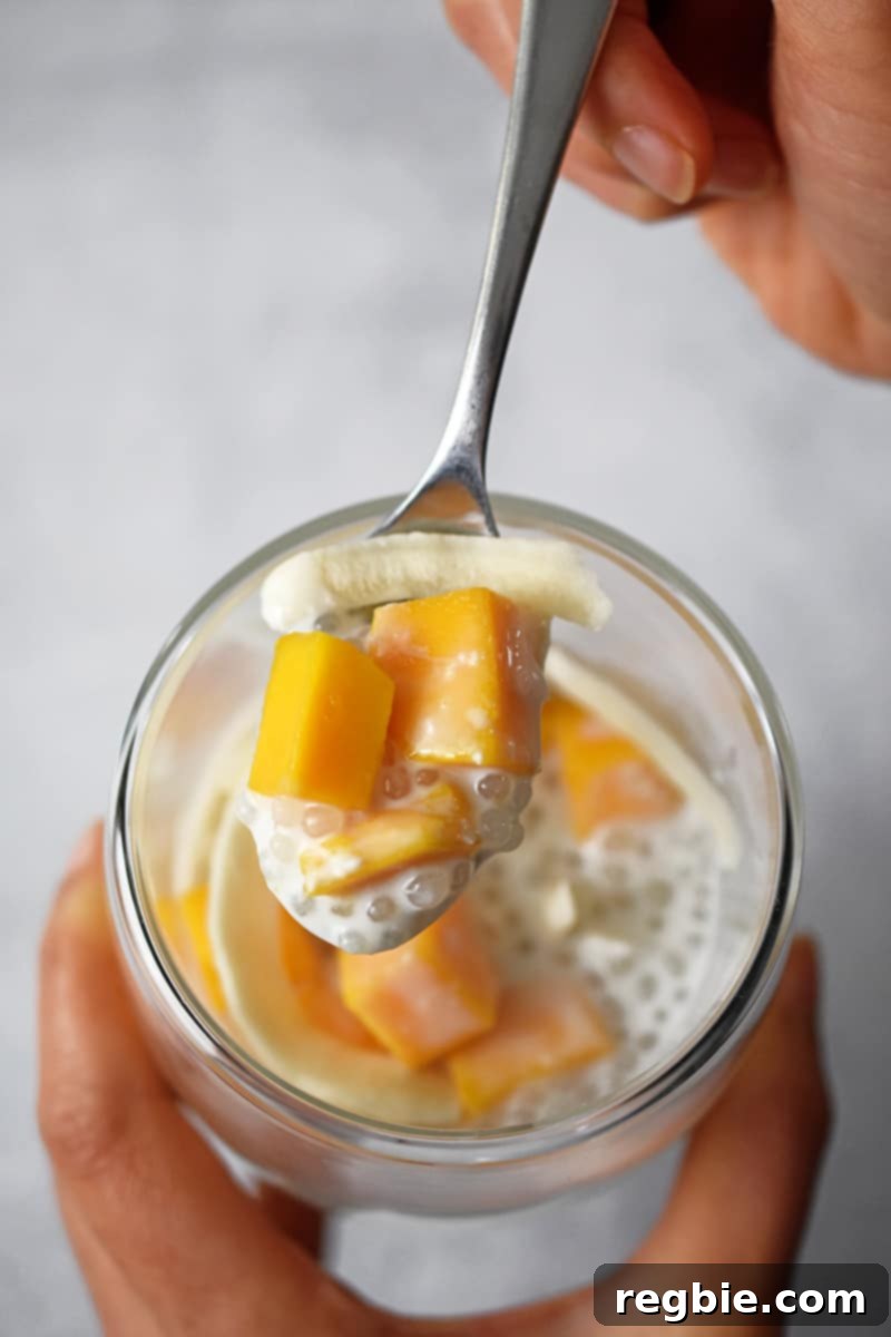 Tropical Mango Coconut Tapioca 3 An overhead shot of someone taking a spoonful of mango sago from a clear glass.