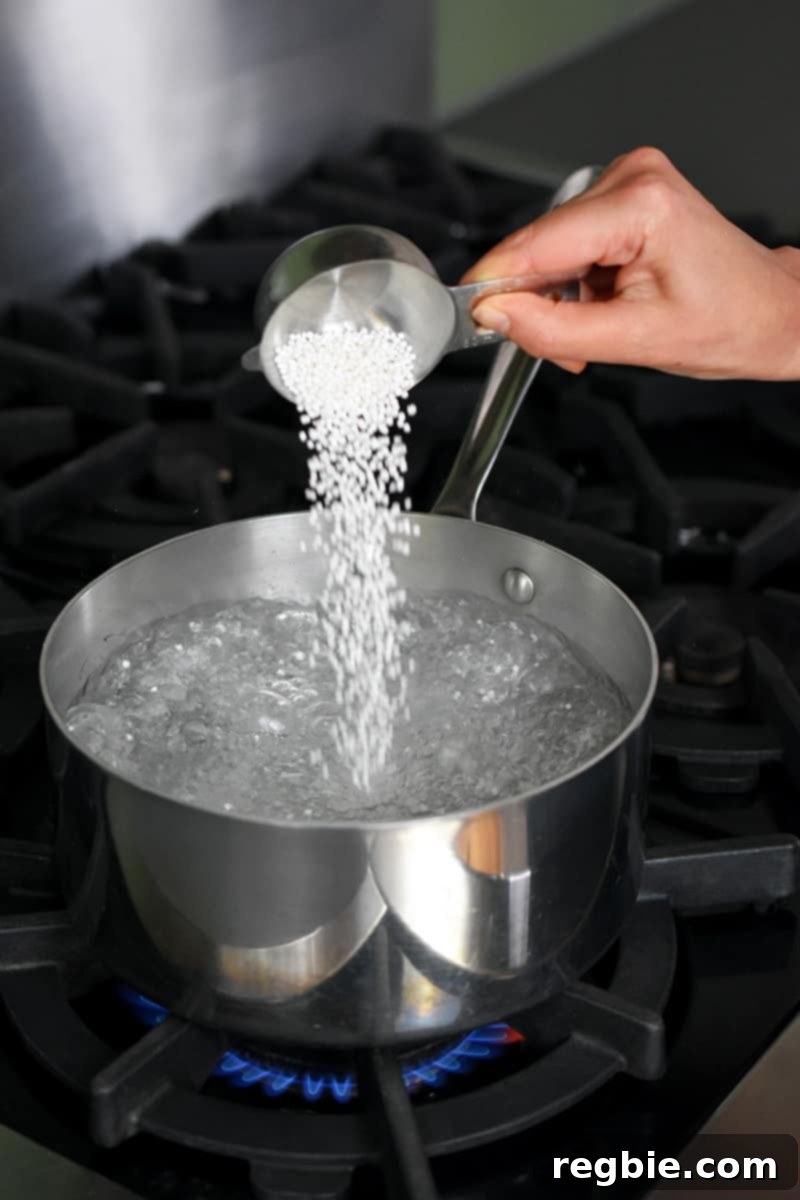 Tropical Mango Coconut Tapioca 7 A hand is adding small tapioca pearls into a saucepan filled with boiling water.