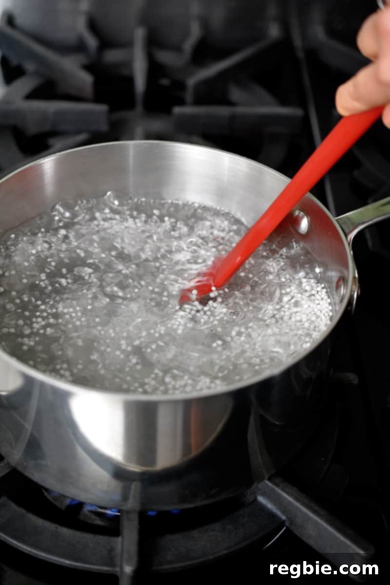Tropical Mango Coconut Tapioca 8 A closeup of a large saucepan filled with boiling water and small tapioca pearls. A red spatula is stirring the contents of the pan.