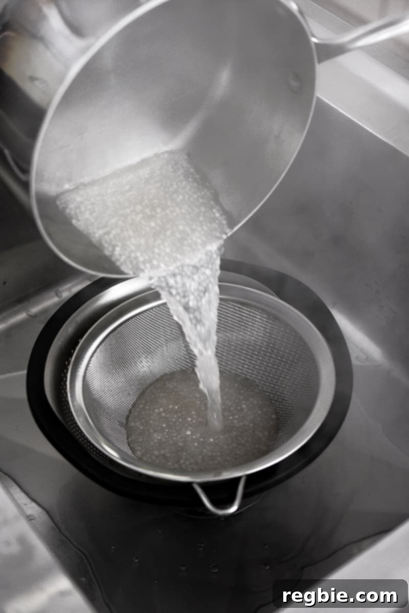 Tropical Mango Coconut Tapioca 10 A closeup of a saucepan pouring cooked small tapioca pearls into a fine mesh sieve in a colander.