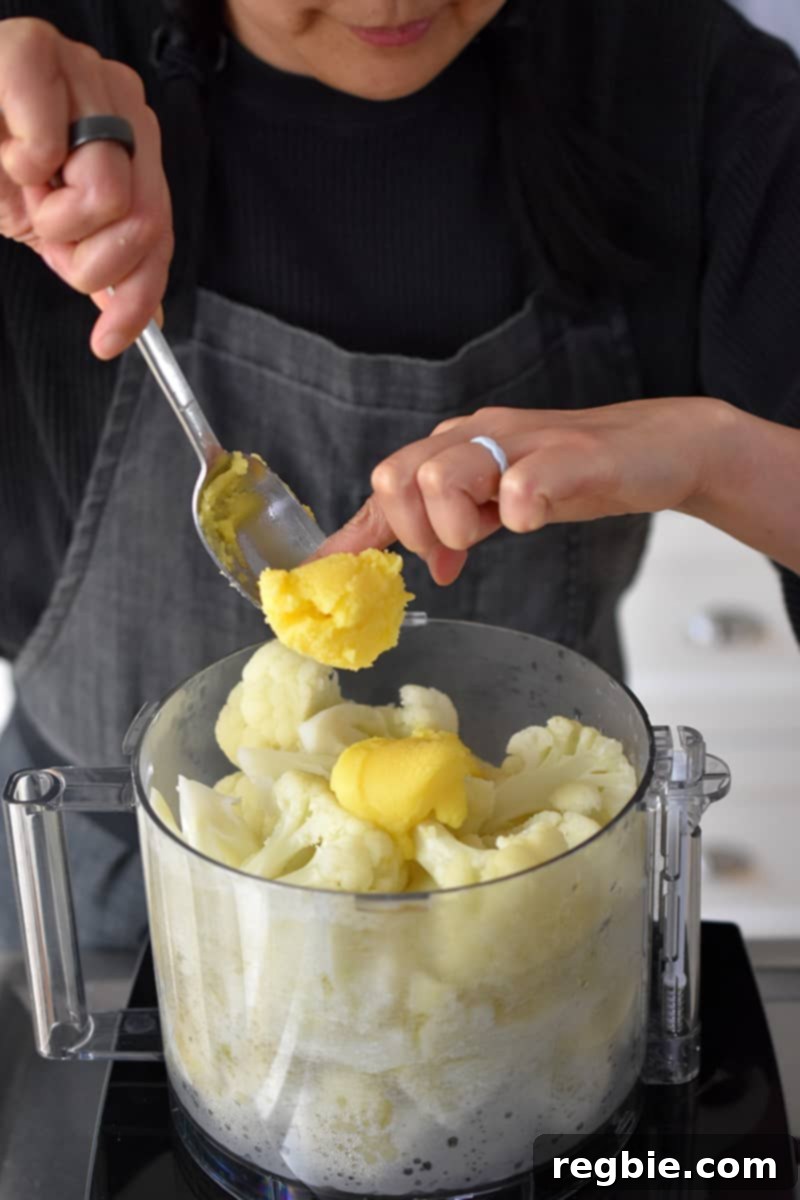 Garden Colcannon 14 Adding ghee to an open food processor with cooked cauliflower florets.