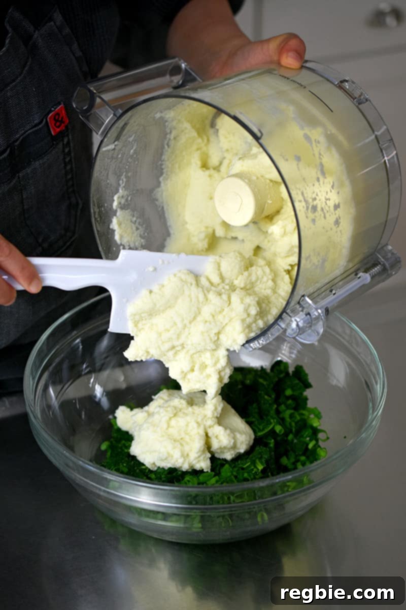 Garden Colcannon 16 Using a white spatula to spoon cauliflower puree into a large bowl filled with chopped kale and scallions.