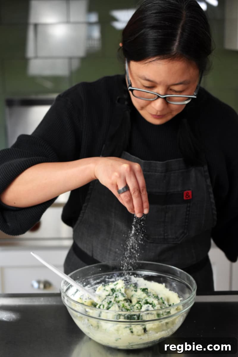 Garden Colcannon 17 An Asian woman in glasses is sprinkling salt on some cauliflower colcannon in a bowl.