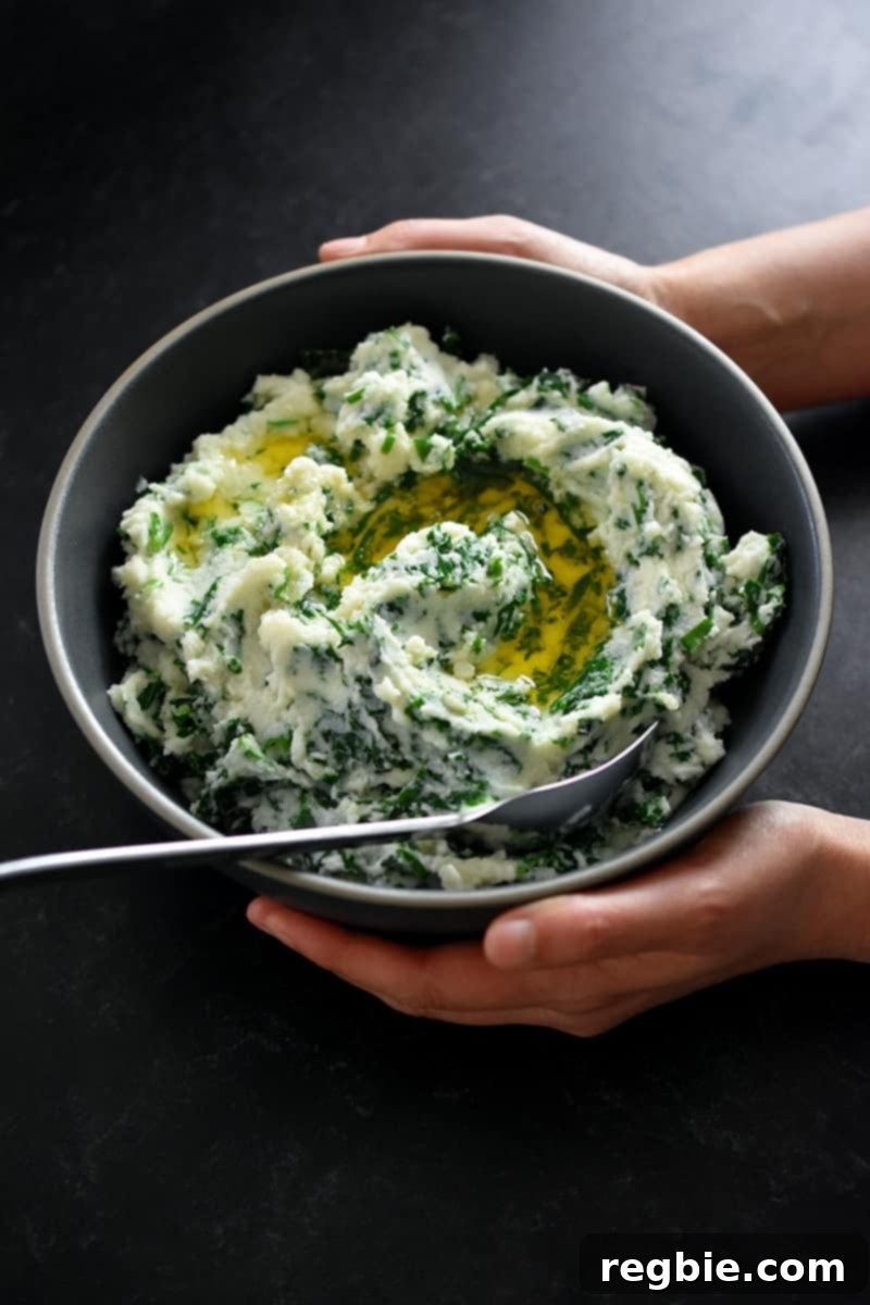 Garden Colcannon 19 Two hands are holding a gray bowl filled with cauliflower colcannon with a swirl of melted ghee inside.