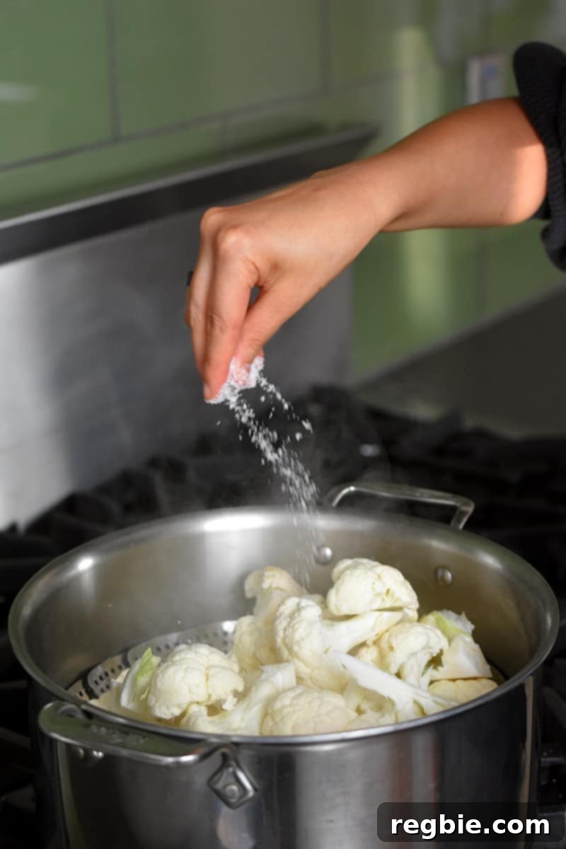 Garden Colcannon 6 A hand is sprinkling salt into an open stockpot filled with cauliflower in a steamer.