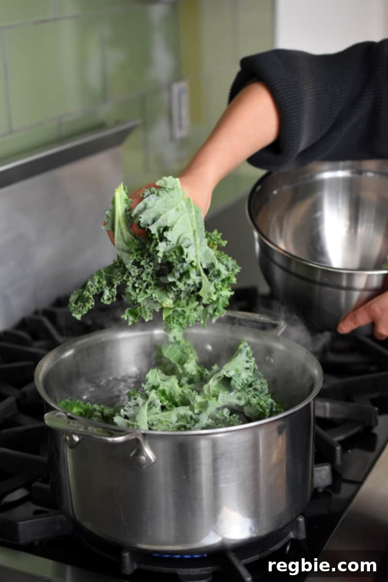 Garden Colcannon 7 A hand is adding curly kale into a open pot of salted water on stovetop.