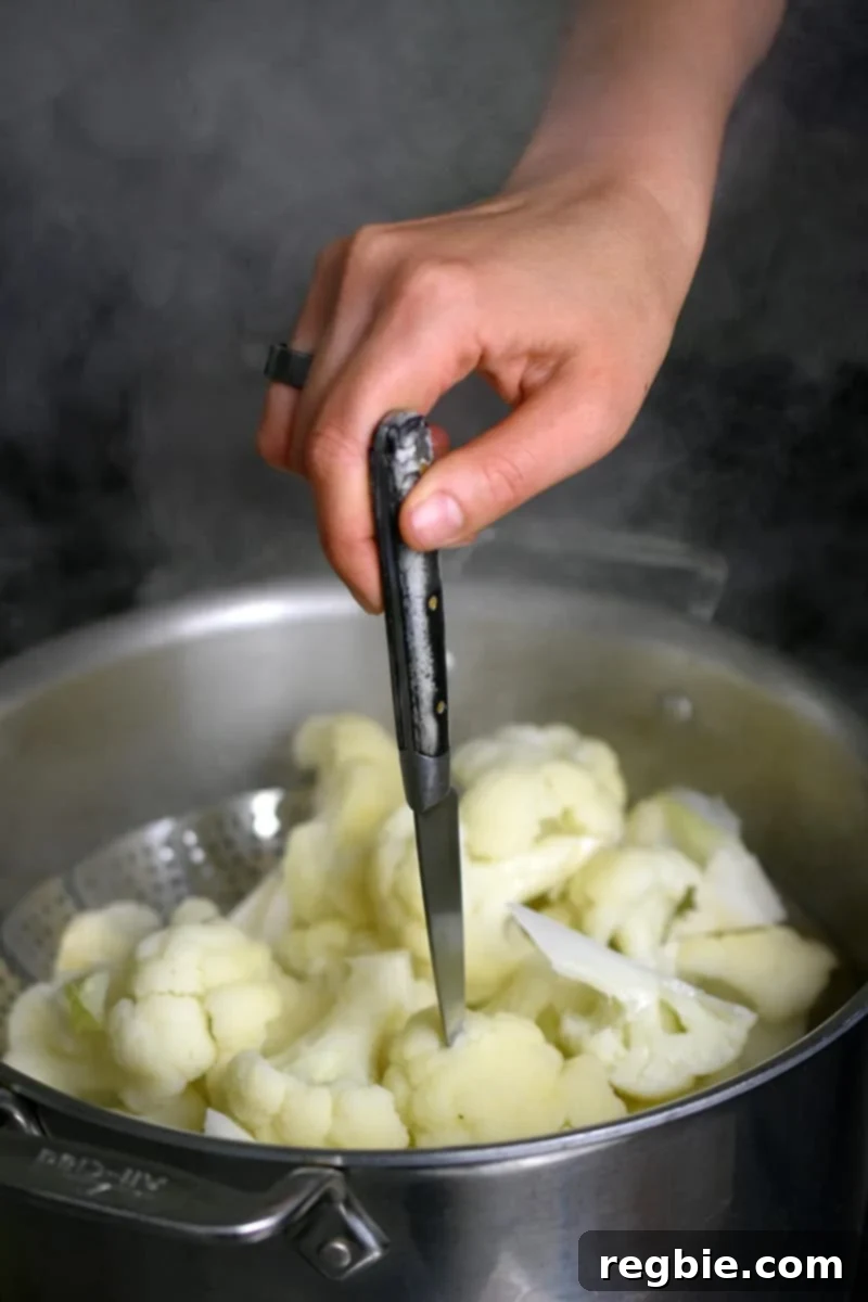 Garden Colcannon 10 A hand is using a paring knife to pierce a pice of steamed cauliflower in an open stockpot to see if it is ready.