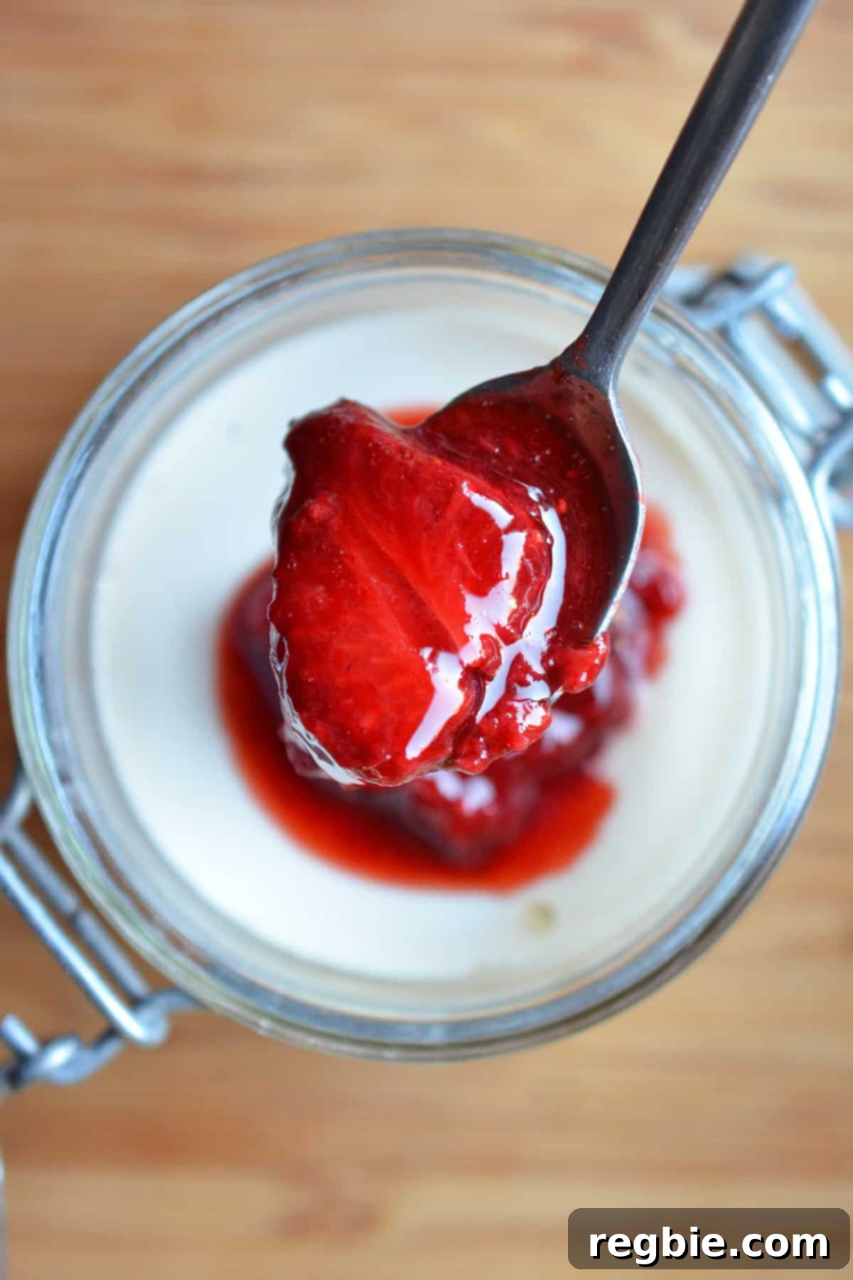 An overhead shot of strawberry Panna Cotta in a jar with a spoon lifting some up.