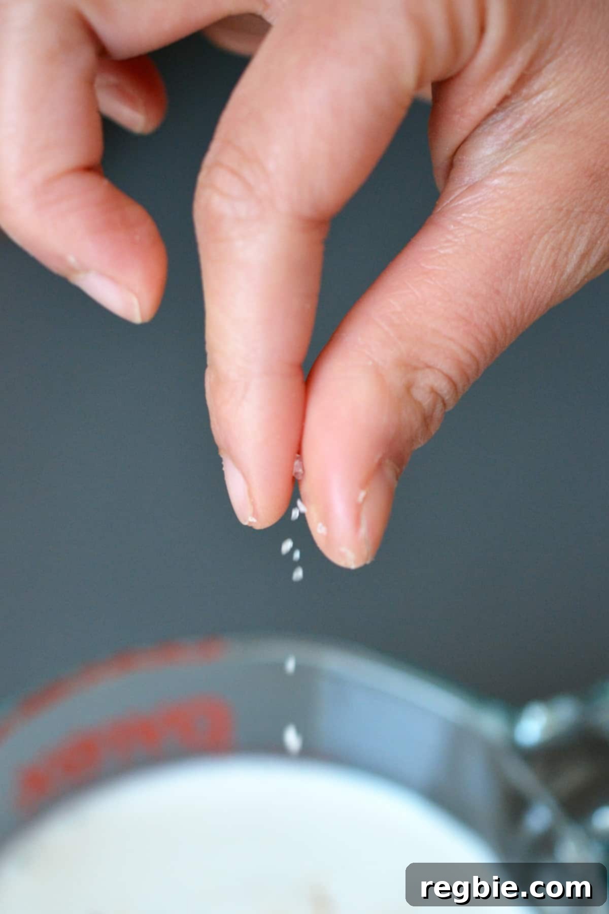 Adding a pinch of salt to a measuring cup filled with panna cotta mixture.