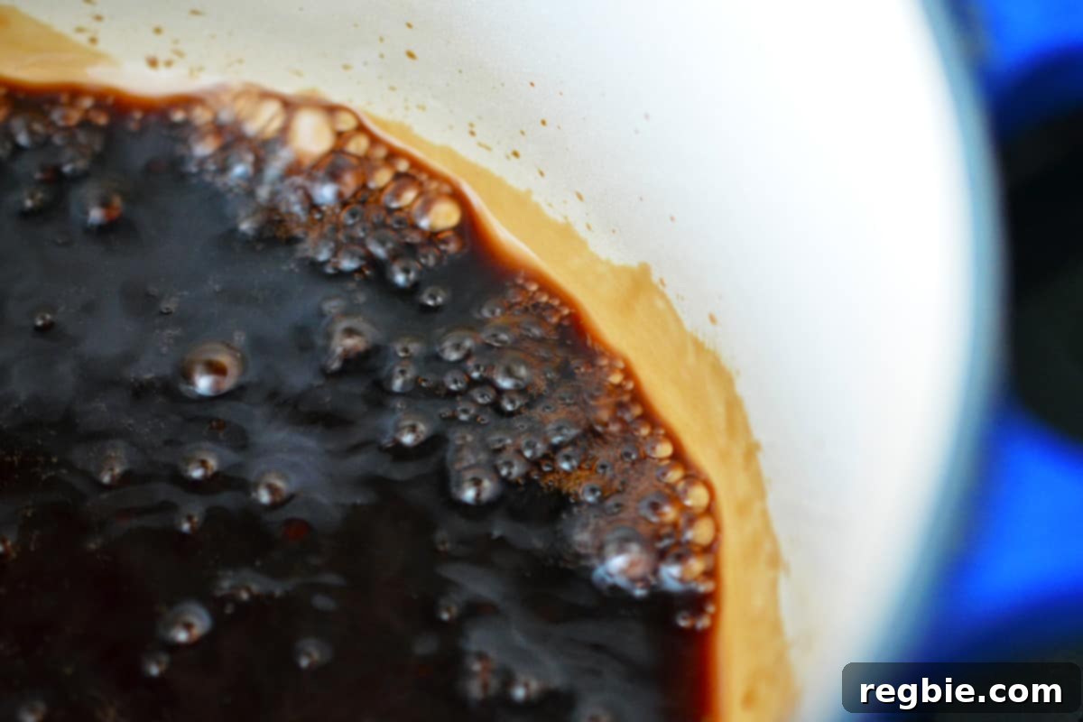 A closeup shot balsamic vinegar simmering and reducing in a cast iron sauce pan.