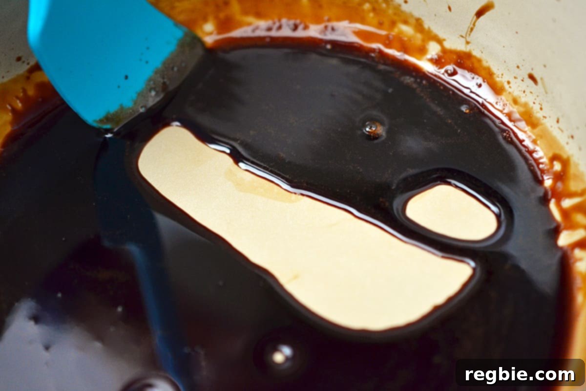 Reduced balsamic vinegar in a sauce pan where a blue silicone spatula shows how thick it is when dragged across the bottom of the pan.