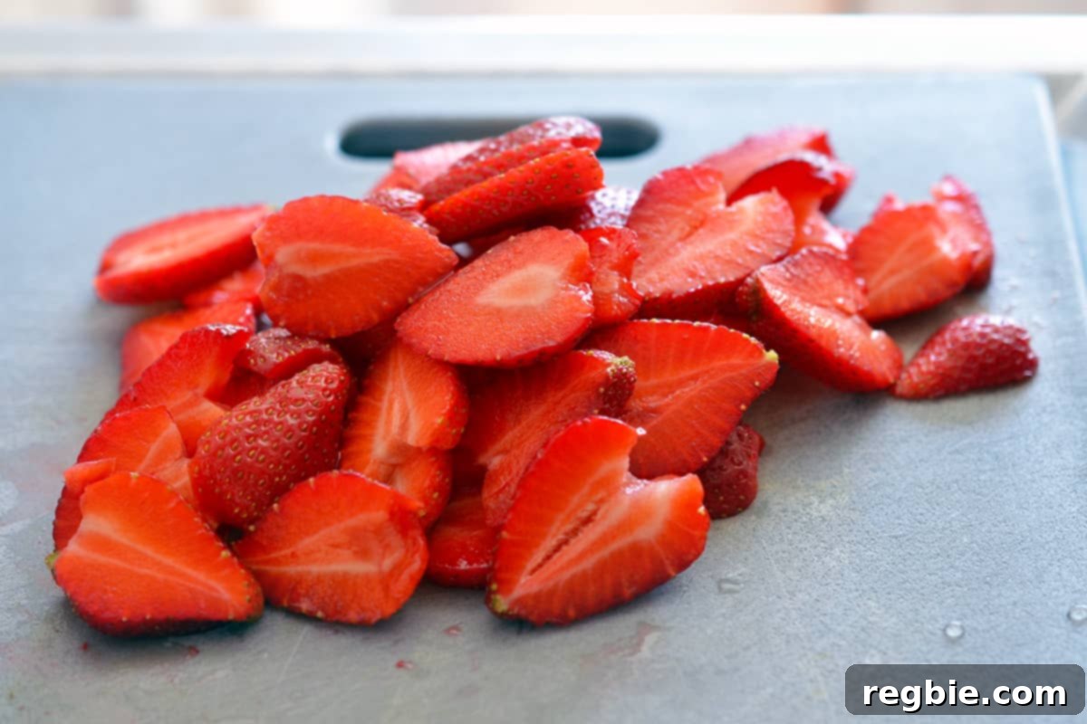 A pile of sliced strawberries on a gray cutting board.