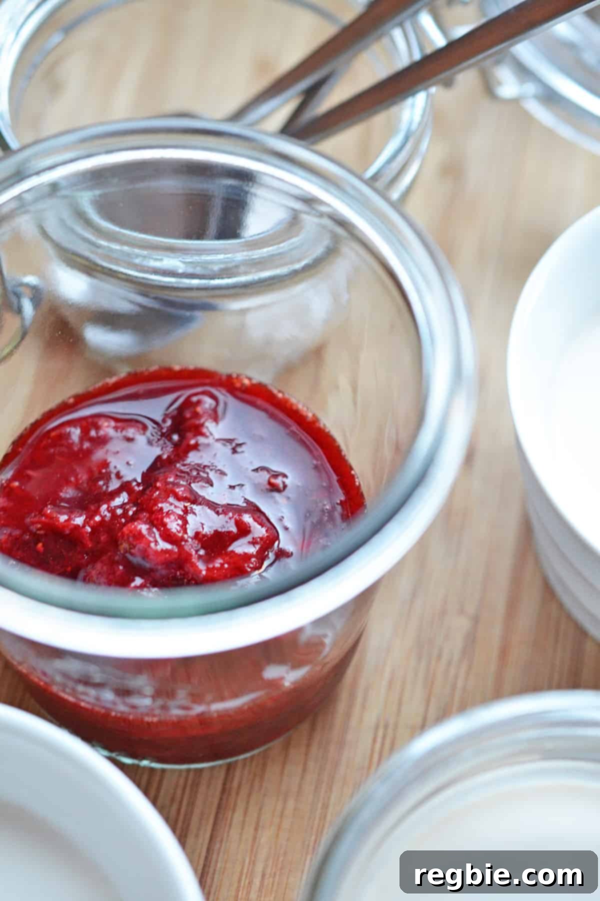 A closeup shot of a jar of homemade strawberry compote next to ramekins filled with Panna Cotta.
