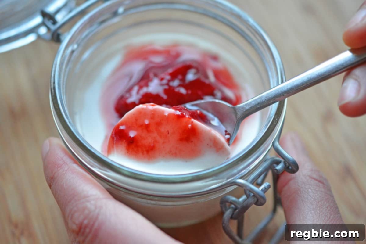 Scooping out a spoonful of strawberry Panna Cotta from a glass jar.