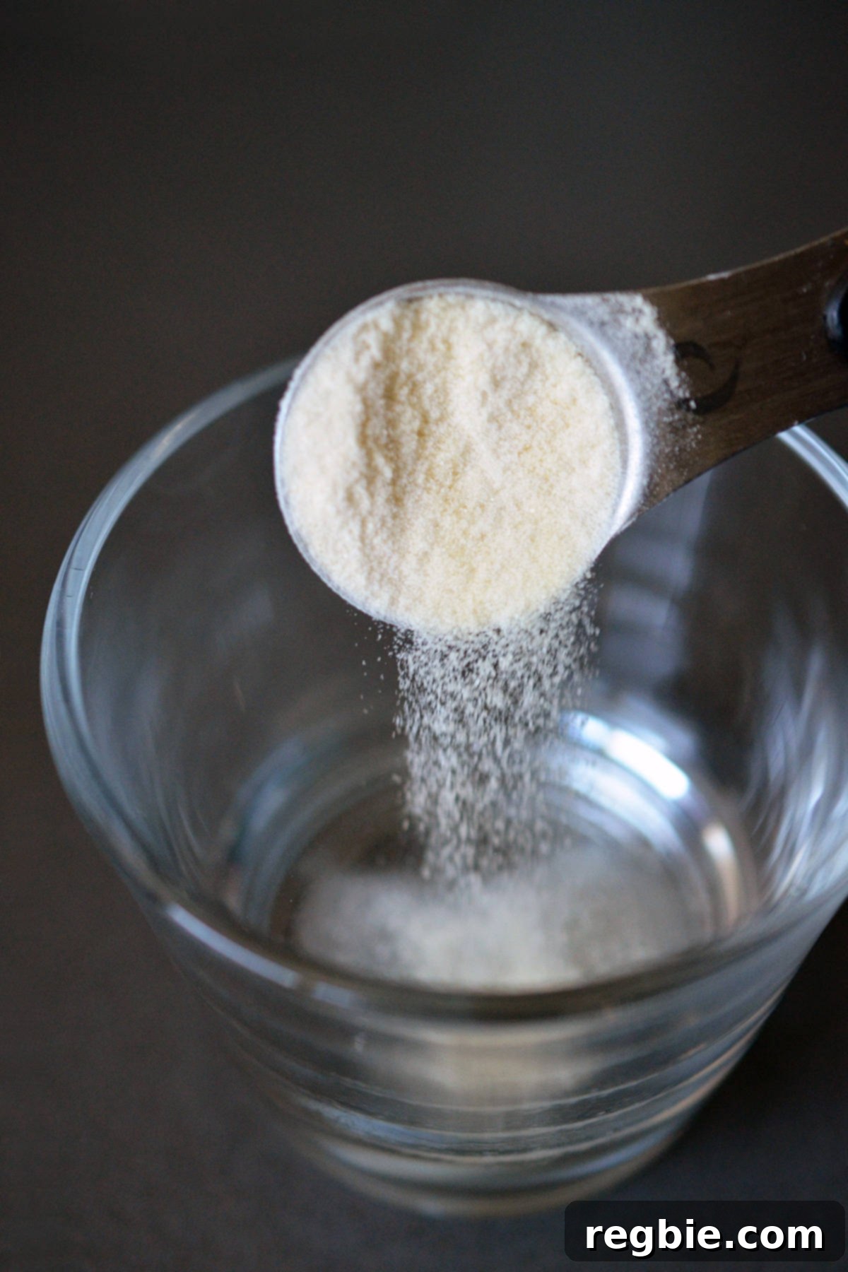 Adding a spoonful of powdered gelatin into a small bowl filled with liquid.