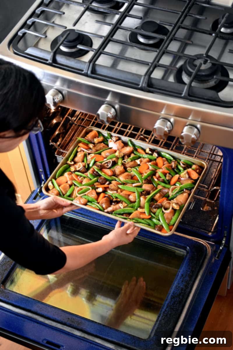 One-Pan Wonder Chicken Stir-Fry 11 An Asian woman is bending down to place a sheet pan filled with chicken and vegetables into an open oven.