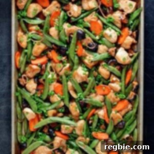 An overhead shot of sheet pan chicken stir-fry right out of the oven. Two hands are holding the edges of the pan with blue and white towels.