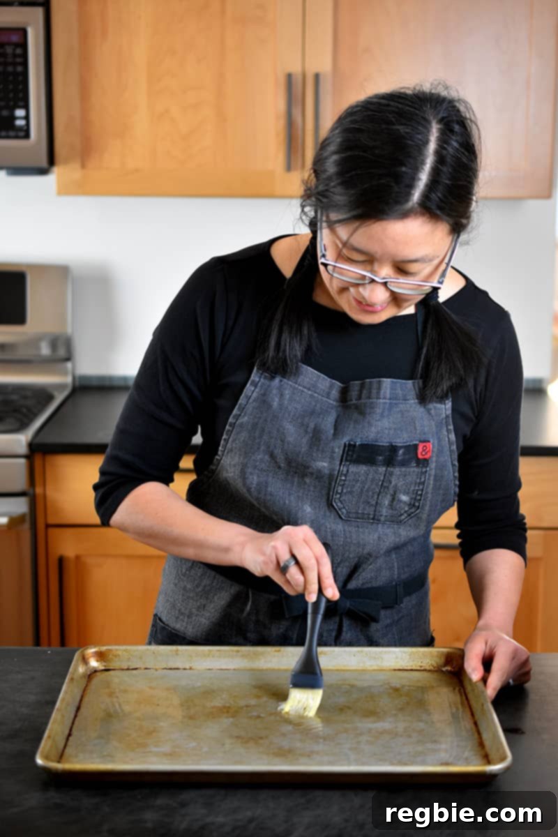 One-Pan Wonder Chicken Stir-Fry 9 A brunette Asian woman is brushing avocado oil on a rimmed baking sheet.