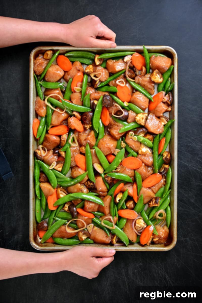 One-Pan Wonder Chicken Stir-Fry 10 An overhead shot of a sheet pan filled with uncooked stir-fry chicken and vegetables in a single layer.