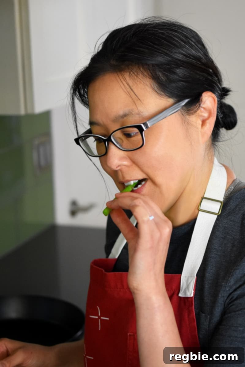 Whole30 Keto Paleo Asparagus Mimosa 11 An Asian woman in a red apron is biting on a piece of asparagus.