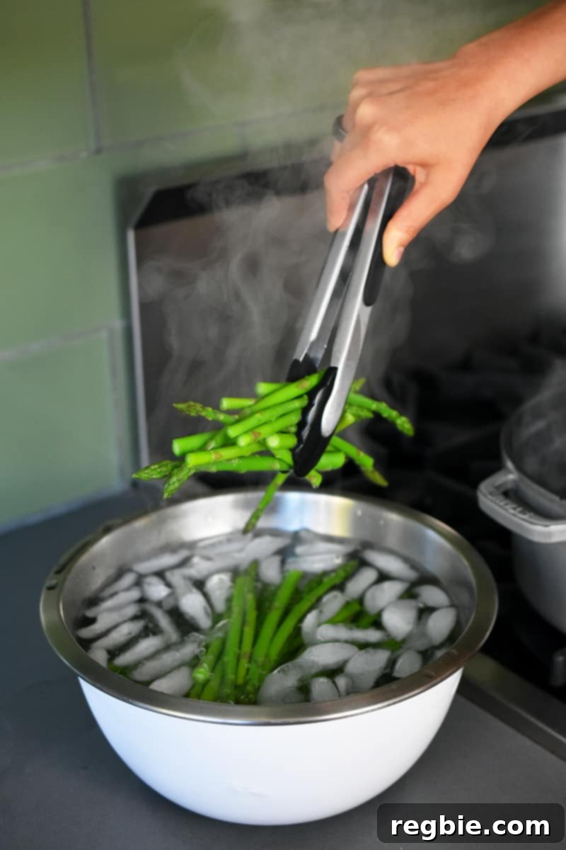 Whole30 Keto Paleo Asparagus Mimosa 12 Someone using tongs to place cooked asparagus into a large bowl of ice water.